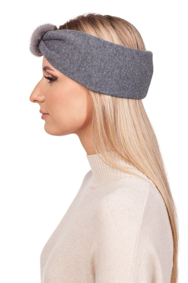 A woman with long blonde hair is wearing the Grey Cashmere Headband with Mink Fur by FurbySD, featuring a chic knotted front and luxurious mink fur accent. She pairs it elegantly with a cream-colored turtleneck sweater as she poses in profile against a white background, highlighting the exquisite craftsmanship from Lithuania.