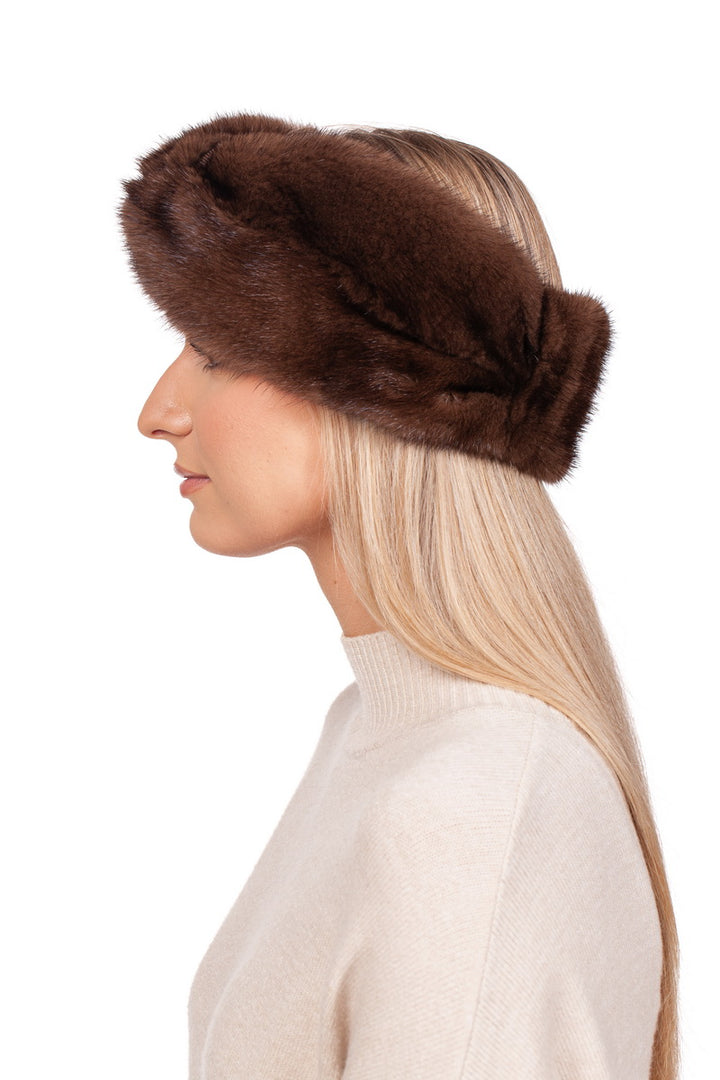 A person with long blonde hair wearing a FurbySD handcrafted brown mink fur headband and a beige sweater is viewed in profile against a white background.