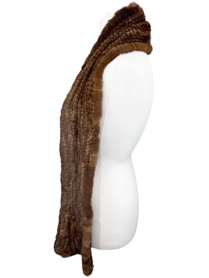 A luxurious brown knitted mink fur scarf from FurbySD is draped elegantly over the shoulder of a white mannequin, shown in side profile against a plain white background. The ethically sourced fur ensures a soft, plush appearance that adds sophistication.