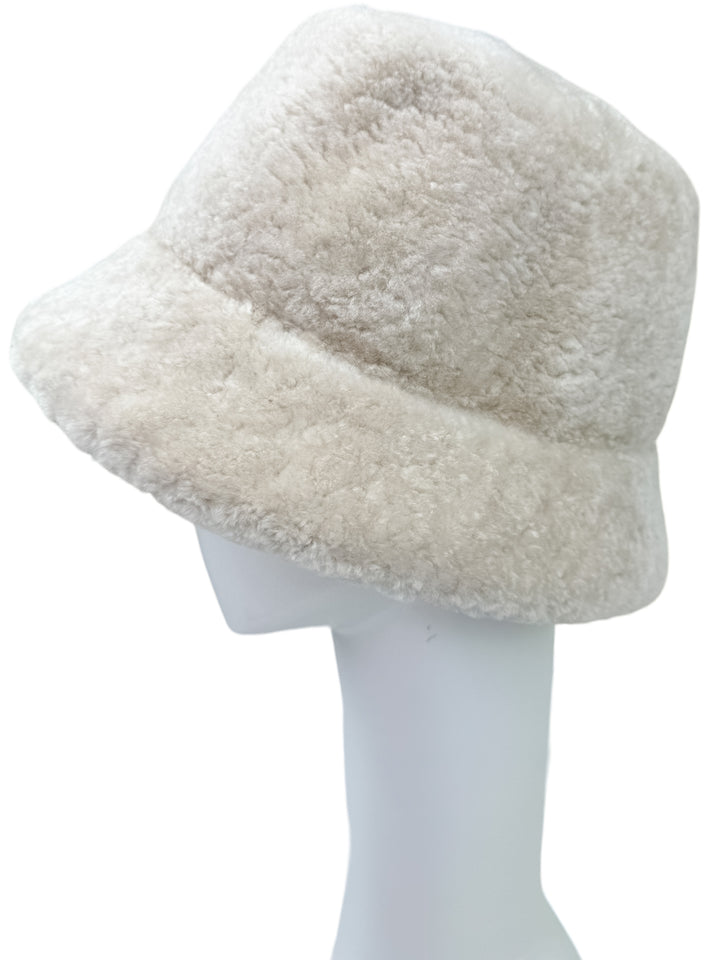 The Pearl White Astrakhan Fur Bucket Hat by FurbySD is showcased on a white mannequin head set against a simple background. This hat, with its wide and soft brim, has an Astrakhan fur-like textured surface that adds to its cozy look.