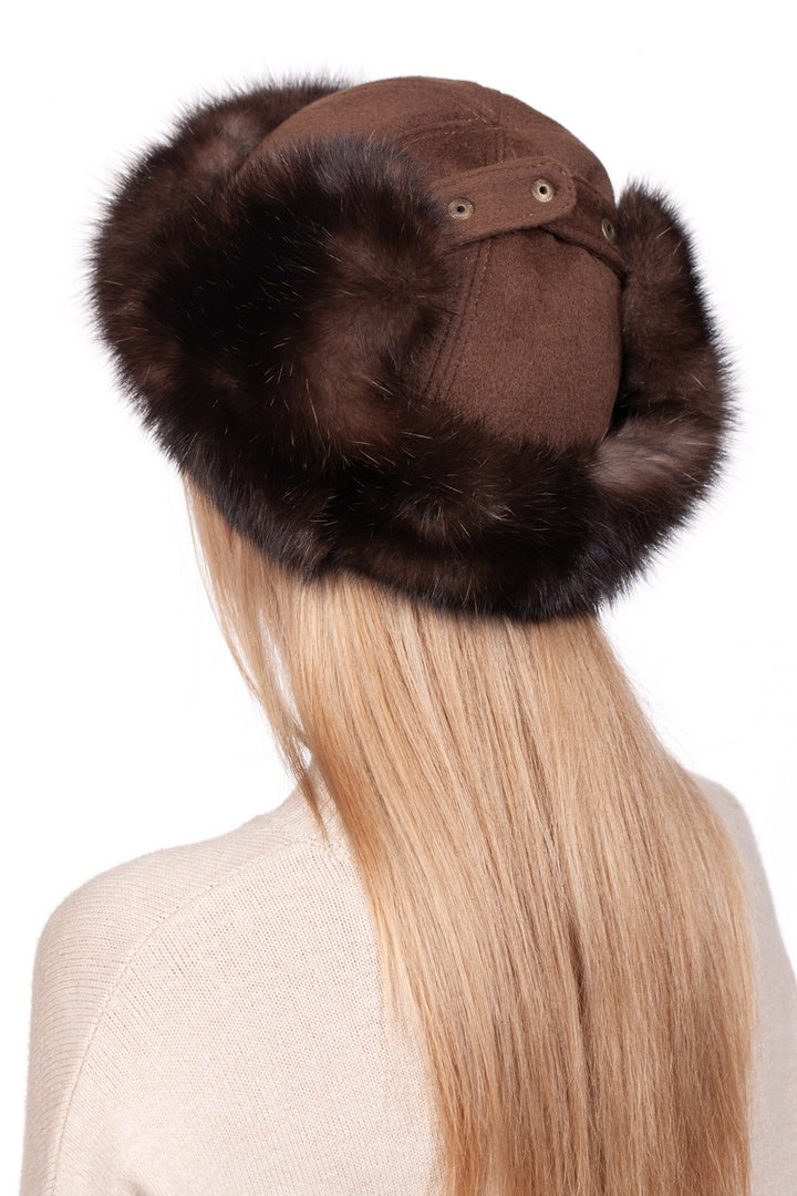 Someone with long blonde hair is wearing a stylish winter accessory from FurbySD—a Brown Barguzin Sable Fur Ushanka Hat. They are also dressed in a light beige sweater and are shown from behind against a plain white background.