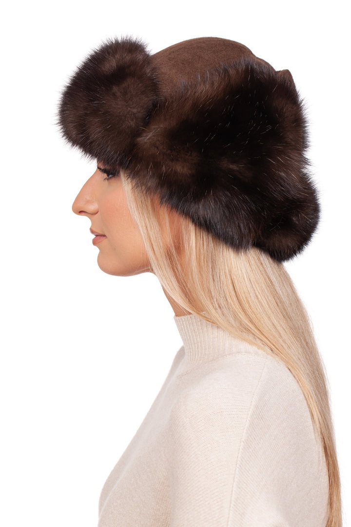 A woman in profile wears a chic FurbySD Brown Barguzin Sable Fur Ushanka Hat, perfectly paired with a cream sweater. Her long, straight blonde hair flows elegantly beneath this stylish winter accessory.