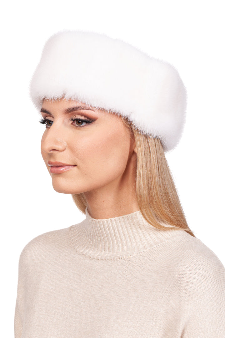 A woman wearing a FurbySD White Mink Fur Headband and a beige turtleneck sweater looks to the side against a white background.