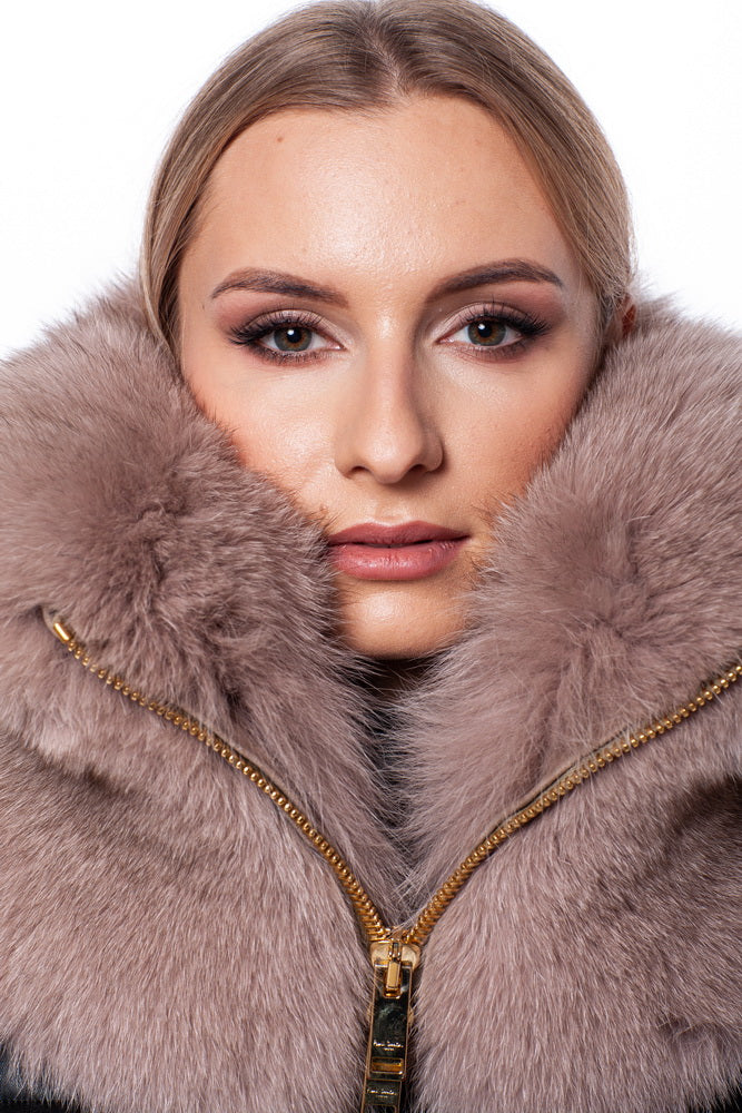 A woman with light skin and blonde hair looks directly at the camera. She is wearing a coat featuring FurbySD's large, luxurious Fox Fur Zipped Collar Scarf that frames her face. The collar is partially zipped up, and she has a neutral makeup look with subtle eye shadow.