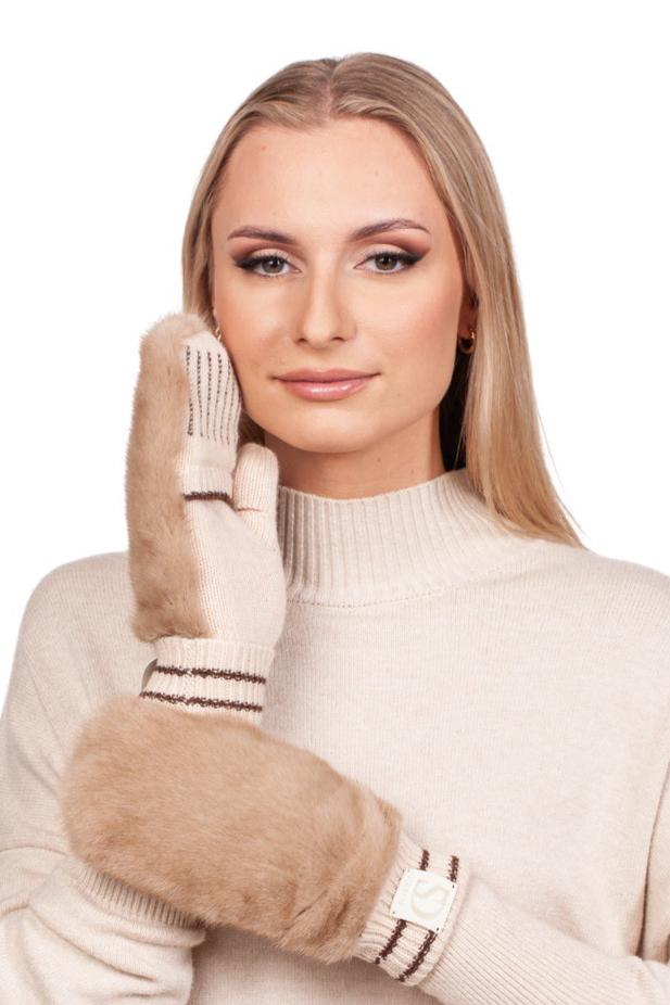 A woman with long blonde hair elegantly poses against a plain white backdrop, wearing a beige knit sweater and showcasing her winter accessory: the Beige Flip Top Mink Fur Mittens by FurbySD. One mitten adorns her hand while the other rests gently against her face, highlighting the mittens' light brown color and striped cuffs.