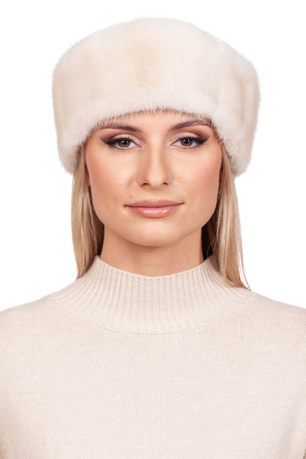 A woman with long blonde hair, dressed in a cream turtleneck sweater and the Pearl Mink Fur Headband by FurbySD, gazes at the camera with a neutral expression. Her luxury winter look is complemented by the cashmere wool mittens from the same set, standing out against the plain white background.