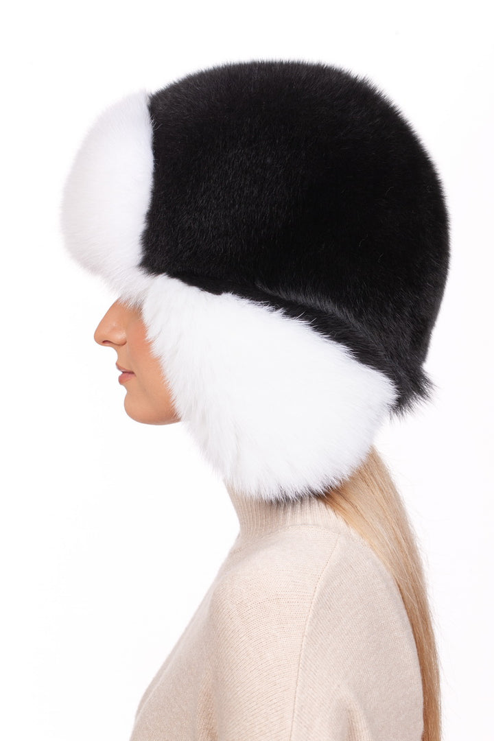 The image shows an individual wearing a FurbySD Fox Fur Ushanka Trapper Hat, featuring large fluffy black and white fox fur. Their long blond hair cascades over a light beige sweater against a plain white background.