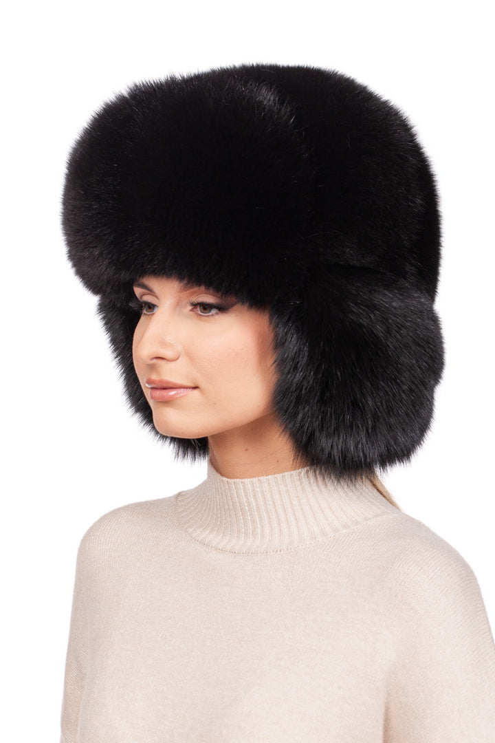 A person models the chic Black Fox Fur Ushanka Trapper Hat by FurbySD, a large and fluffy winter accessory that envelops their head and ears in luxurious black fox fur. They pair it perfectly with a light beige sweater against a simple white background.