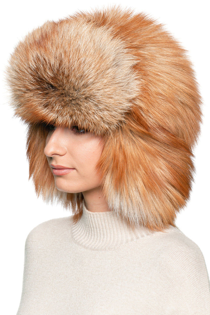 Angled front view of red fox fur trapper hat, luxury Russian ushanka with oversized fluffy fur earflaps and warm lining.