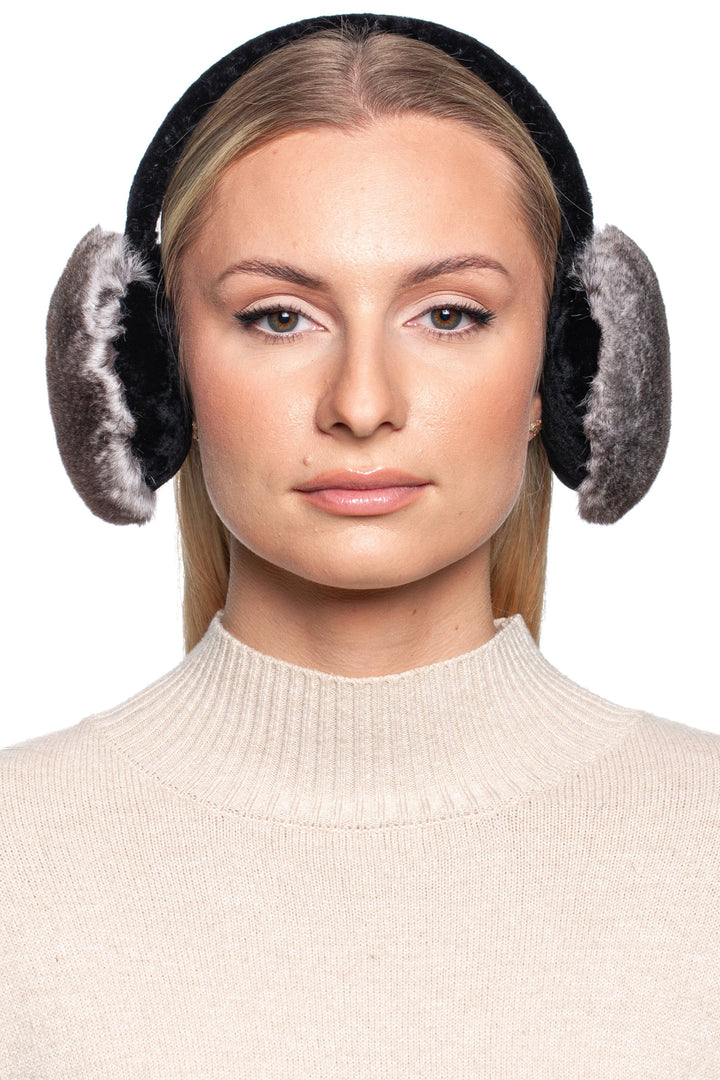 Woman wearing grey rex rabbit fur earmuffs with astrakhan lining, styled with a beige turtleneck sweater. The plush fur ear warmers provide a luxurious and elegant winter accessory.