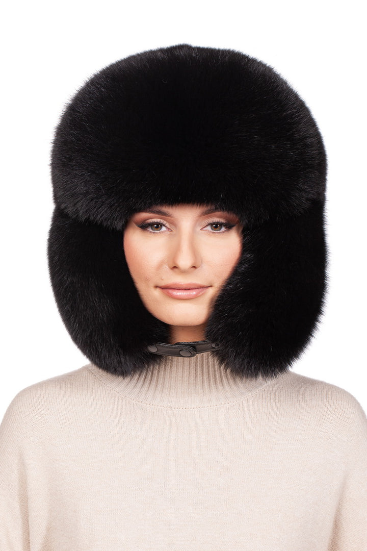 A person dons the Black Fox Fur Ushanka Trapper Hat by FurbySD, a large and fluffy winter accessory made from luxurious black fox fur. They pair it seamlessly with a cozy beige sweater as the hat covers their head and ears. The individual maintains a neutral expression against a plain white background.