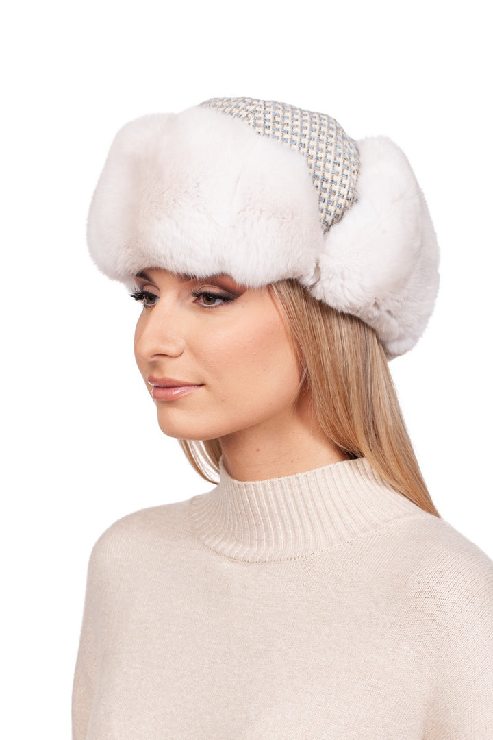 A person with long blonde hair wears the FurbySD Cream White Chinchilla Fur Ushanka Hat, boasting a luxurious white faux fur design with a patterned band. They are dressed in a beige turtleneck sweater and face slightly to the left against a plain white background.