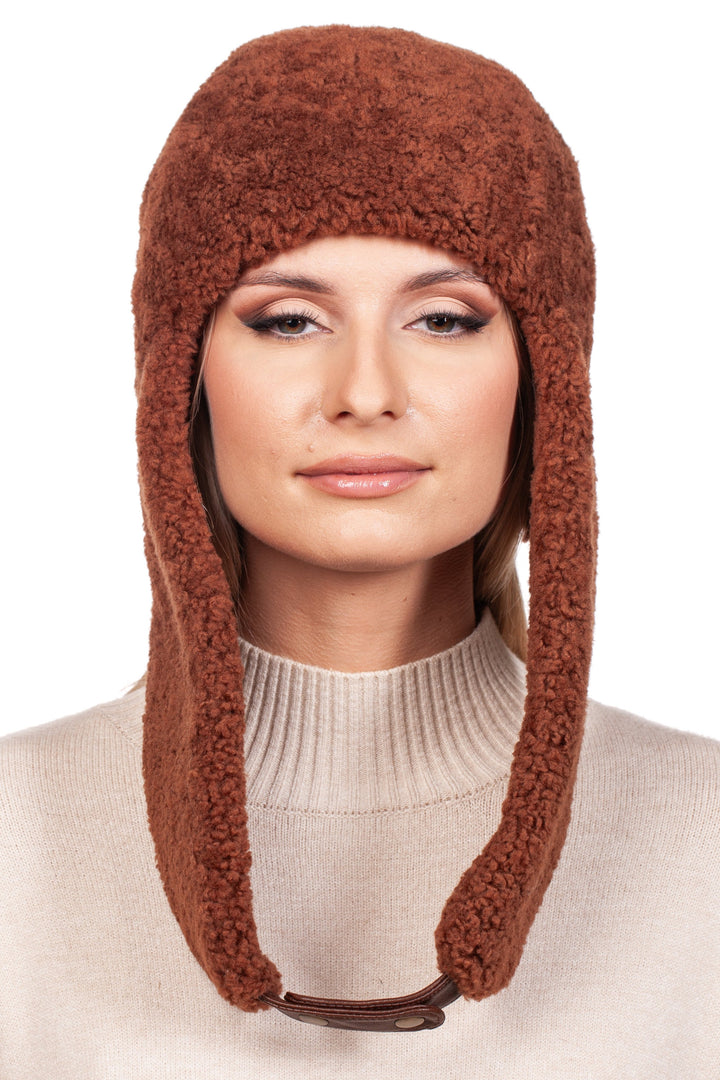 A person is seen wearing the FurbySD Rusty Brown Shearling Fur Earflap Hat, complemented by a beige sweater and neutral makeup. The texture and color of the winter accessory are accentuated against a white background, showcasing its cozy charm.