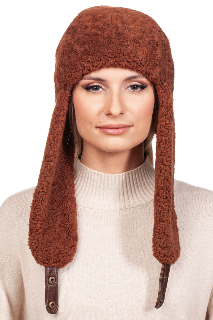 Someone dons the FurbySD Rusty Brown Shearling Fur Earflap Hat, which pairs perfectly with a cream-colored sweater. This winter accessory pops against the plain white backdrop, bringing warmth and style to the ensemble.