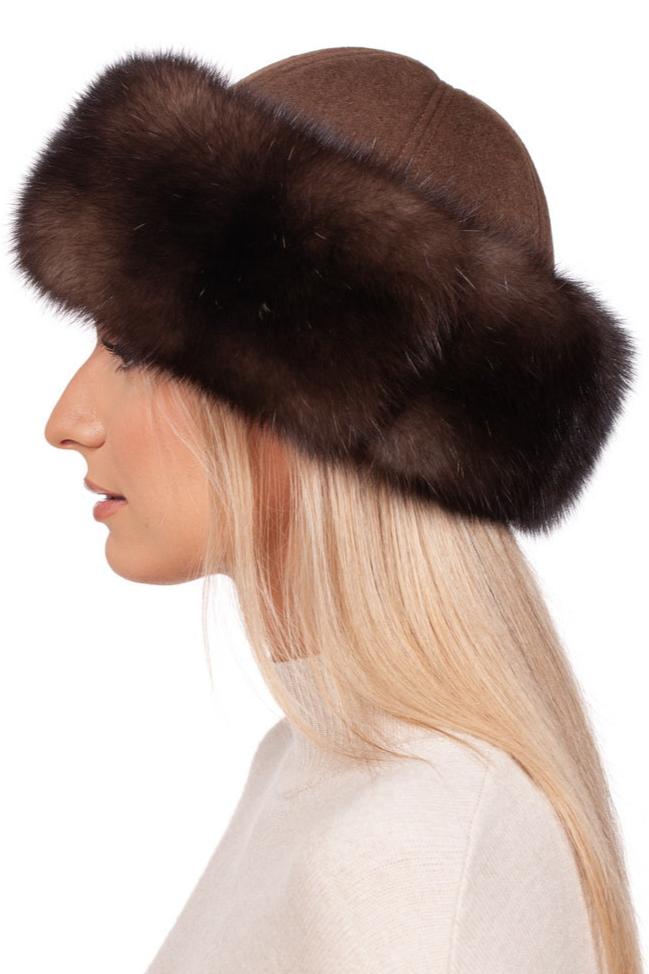 A person with long blonde hair is depicted in profile, wearing the luxurious Brown Sable Fur Roller Hat With Cashmere by FurbySD, featuring a dark trim. They are dressed in a light-colored top against a plain white background.