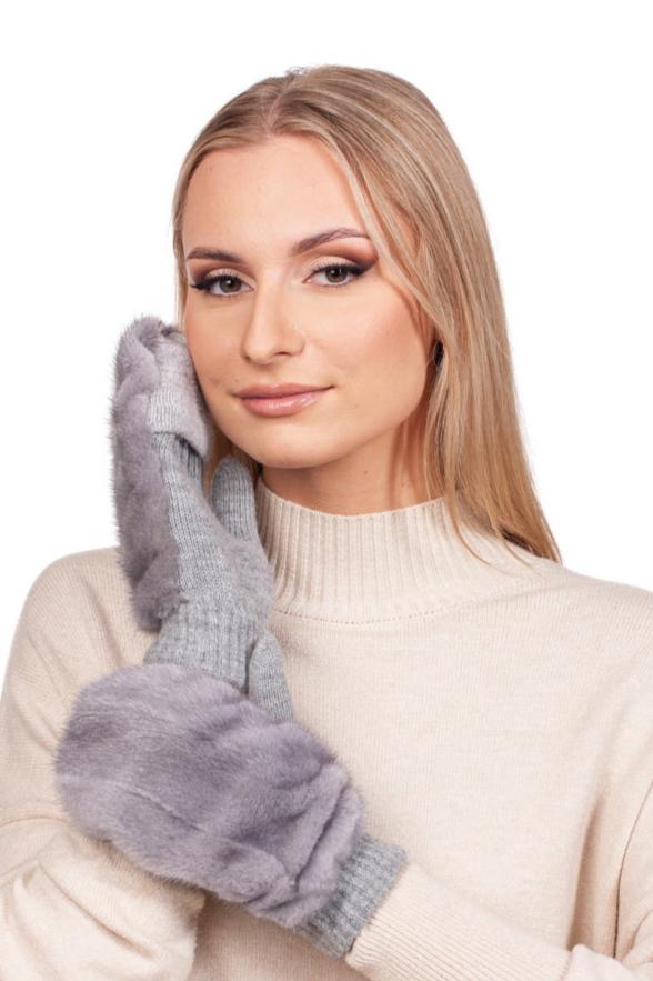 A person with long blonde hair, dressed in a beige sweater, gently holds their face with one hand clad in a Sapphire Mink Fur Flip Top Mitten from FurbySD. The luxurious mink fur mitten enhances their serene smile as they pose against the plain white background.