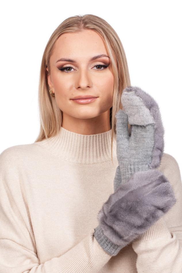 A woman with long blonde hair in a beige sweater holds up her hand, showcasing Sapphire Mink Fur Flip Top Mittens by FurbySD with a soft expression. The background is plain white.