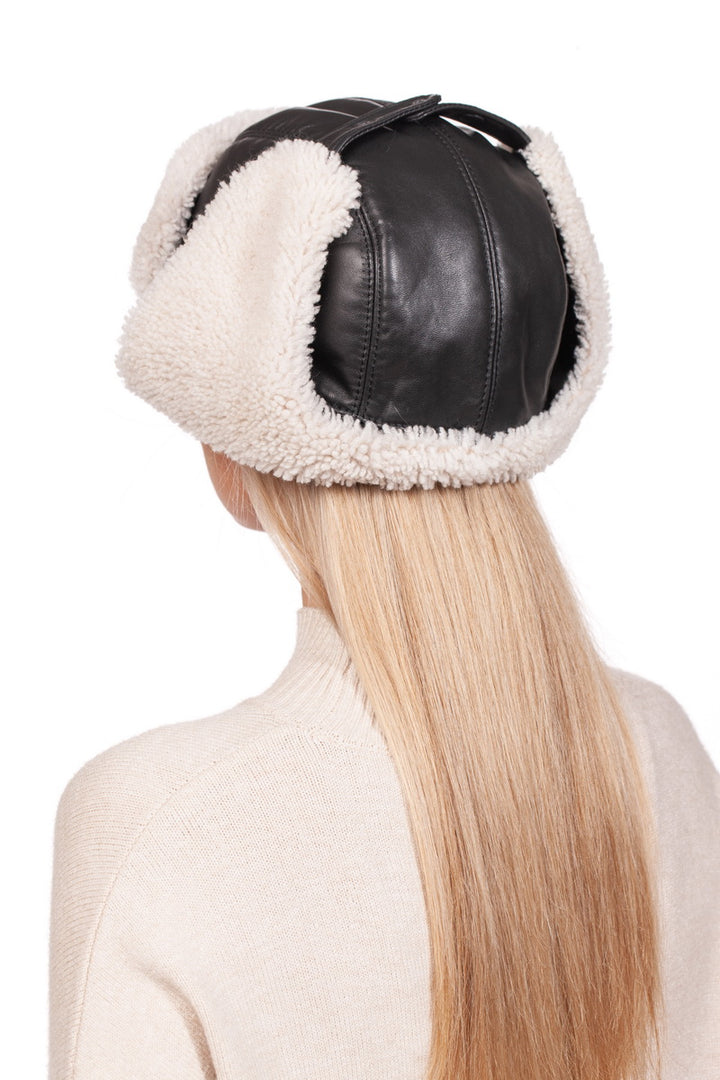 A person with long blonde hair is wearing the White Shearling Fur Aviator Bomber Hat from FurbySD, crafted from black Nappa leather and featuring a fluffy white fleece lining. The back of their sweater stands out against a plain white background.