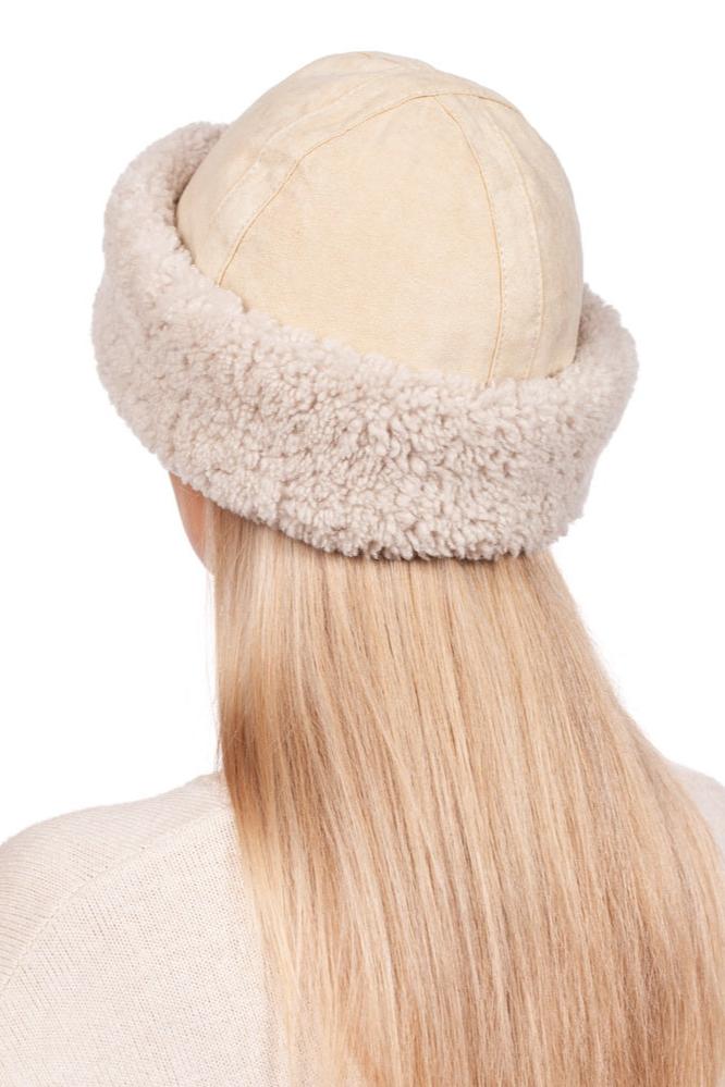 A person with long blond hair is wearing a beige shearling fur hat from the FurbySD set, showcasing its thick, fluffy rim. Photographed from behind against a plain white background, this hat embodies winter fashion accessories.