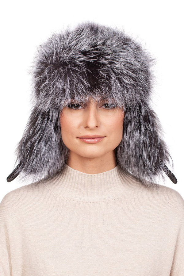 A person wearing the luxurious FurbySD Silver Fox Fur Ushanka Trapper Hat, paired with a beige turtleneck sweater. This fluffy, gray fur hat with ear flaps is impeccably soft and voluminous, enveloping the head and ears. The simple white backdrop enhances the winter luxury feel.