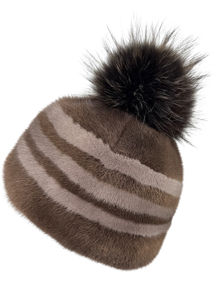 Close-up of striped brown mink fur hat with fluffy fox fur pom pom, luxury handmade winter beanie for women, soft real fur cap with warm design.