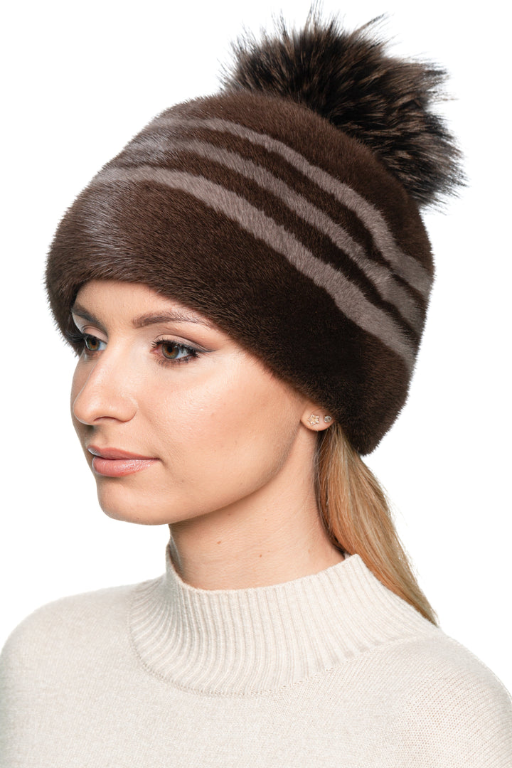 Side angle of women’s striped brown mink fur hat with black fox fur pom pom, elegant luxury beanie for winter city and ski style.