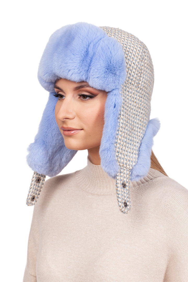 A woman models the Blue Chinchilla Fur Ushanka Hat by FurbySD, featuring stylish ear flaps and plush blue chinchilla fur. She pairs this fashionable piece with a light beige sweater, all set against a plain white background.