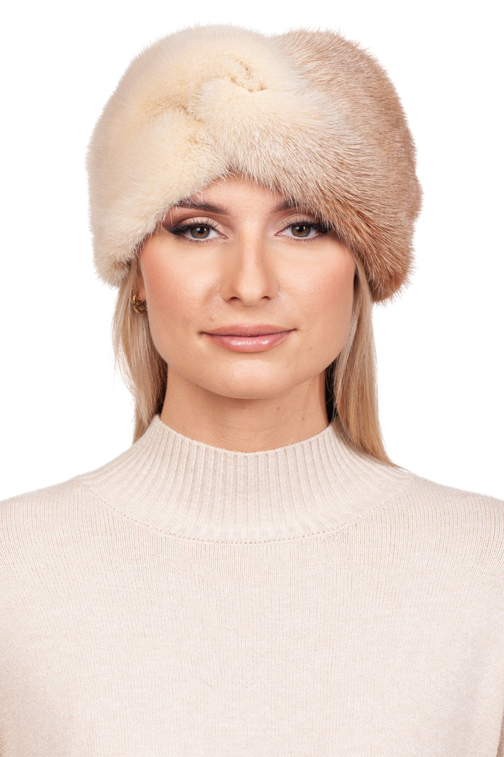 A woman is elegantly dressed in a cream-colored sweater, complemented by a luxurious winter accessory—FurbySD's Two-Tone Beige Mink Fur Headband. She gazes forward against a plain white backdrop, exuding understated charm with her genuine mink fur ensemble.