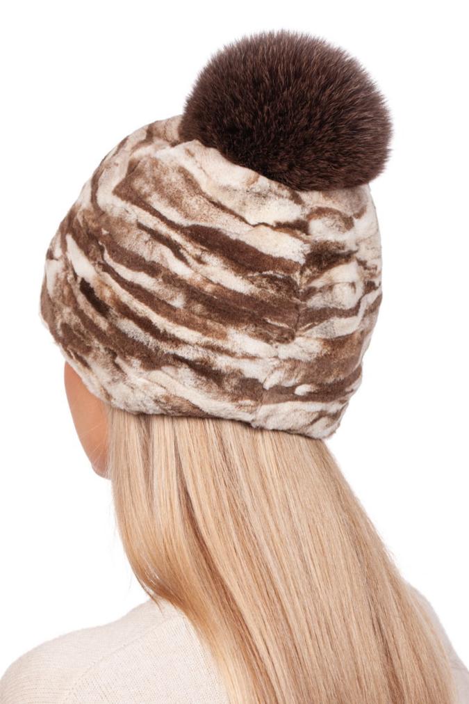 A person with long blonde hair is wearing a FurbySD Beige Sheared Mink Fur Hat With Pom Pom against a plain white background.