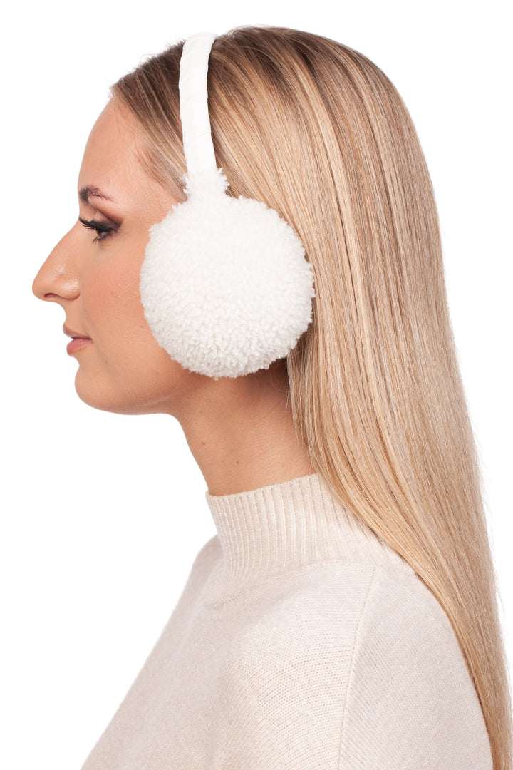 A woman with long blonde hair is wearing FurbySD's White Curly Shearling Fur Earmuffs and a cream-colored sweater. She is facing to the left against a plain white background.