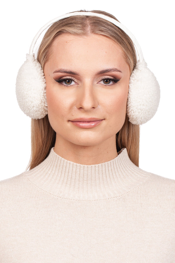 A person with long blonde hair is wearing FurbySD's luxurious White Curly Shearling Fur Earmuffs and a cream-colored turtleneck sweater, smiling slightly against a white background.