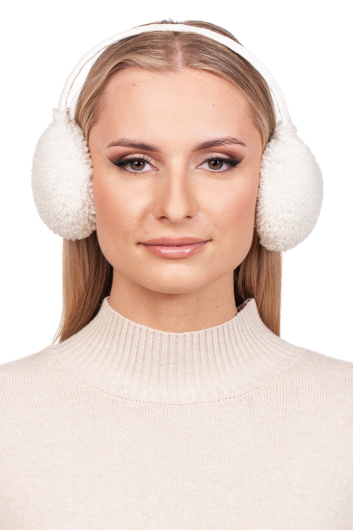 A person with long blonde hair is wearing FurbySD's luxurious White Curly Shearling Fur Earmuffs and a cream-colored turtleneck sweater, smiling slightly against a white background.