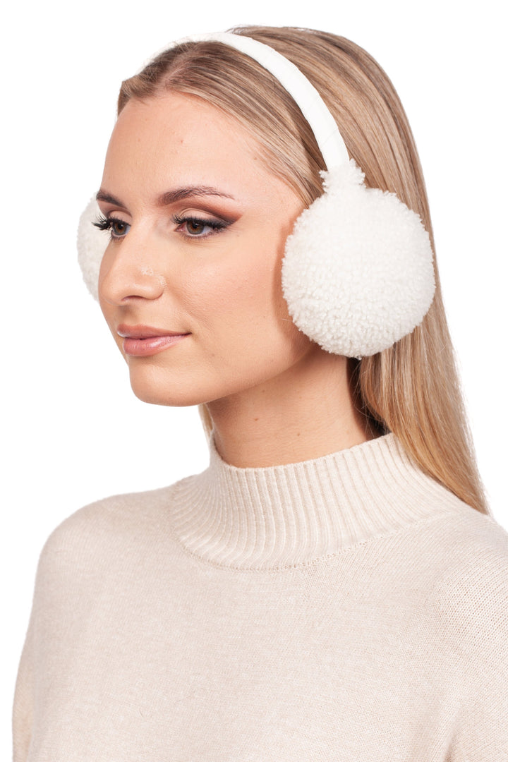 A person with long, blonde hair is wearing FurbySD's White Curly Shearling Fur Earmuffs, paired with a cream-colored turtleneck sweater. They are slightly angled to the left against a plain white backdrop.