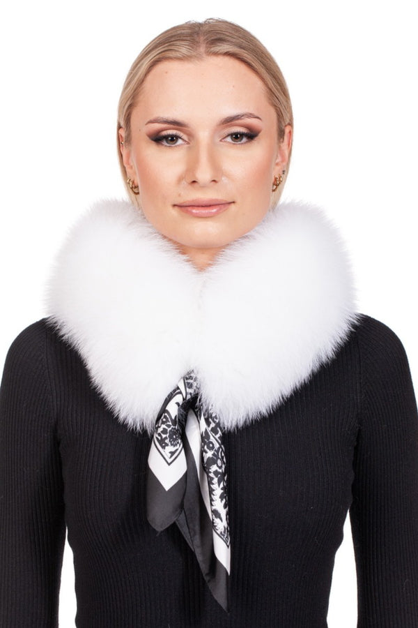 A woman with blonde hair showcases a luxurious handmade fox fur scarf over her black top. The FurbySD White Fox Fur Collar is elegantly tied with a patterned silk ribbon, creating a versatile accessory. She wears subtle makeup and stud earrings against a plain white background.