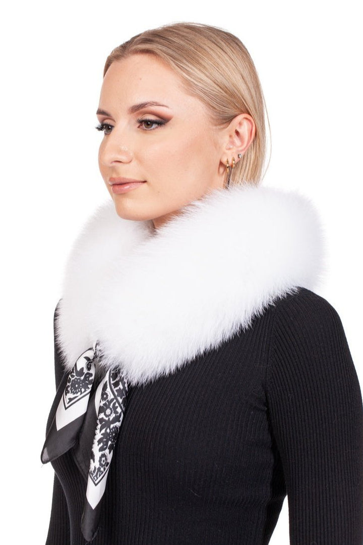 A person with blonde hair sports a fluffy handmade fox fur collar from FurbySD and a sleek black outfit. They accessorize with hoop earrings and enhance their look with a versatile touch—a stylish black-and-white printed scarf. The backdrop is a crisp white.