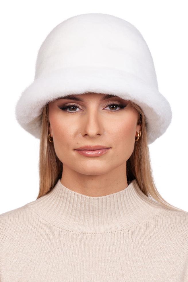 A person with long blonde hair wearing a FurbySD White Mink Fur Bucket Hat and a beige knitted turtleneck sweater. The individual has a neutral expression and is set against a plain white background.