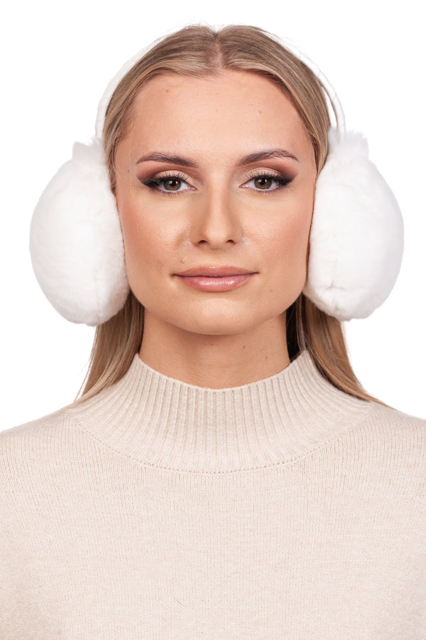 A woman wears the luxurious White Rex Rabbit Fur Earmuffs by FurbySD, paired with a beige turtleneck sweater. Her long blonde hair flows freely, enhanced by subtle eye shadow and lip gloss. The plain white backdrop accentuates her elegant winter style.