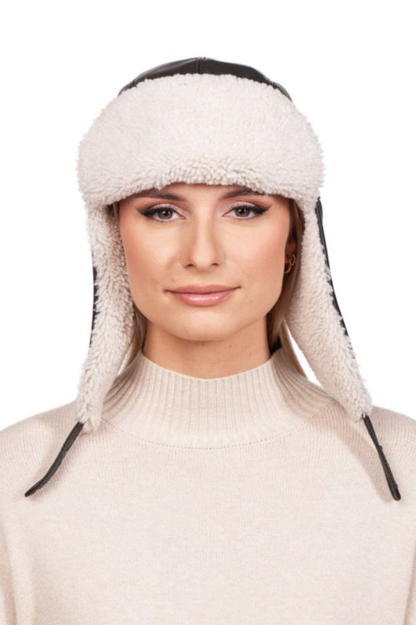 A person, donned in a FurbySD White Shearling Fur Aviator Bomber Hat and a beige sweater, stands against a simple white backdrop, gazing directly at the camera.