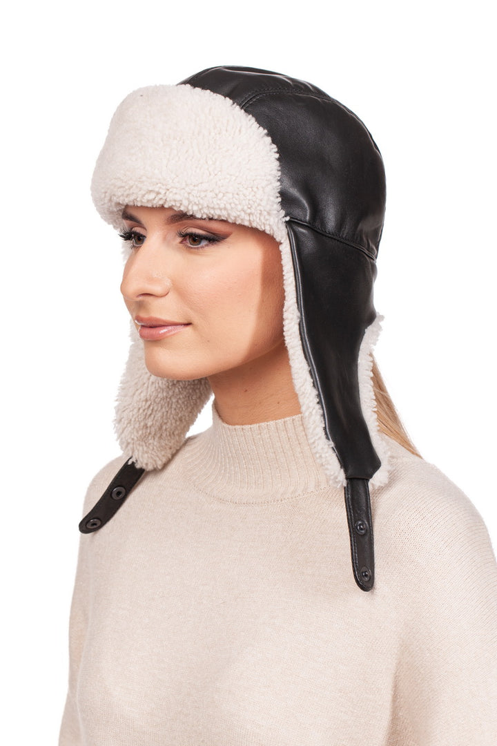 A person wearing a white shearling fur aviator bomber hat by FurbySD, with dark eyeliner and a beige sweater, looks to the side against a plain white background.