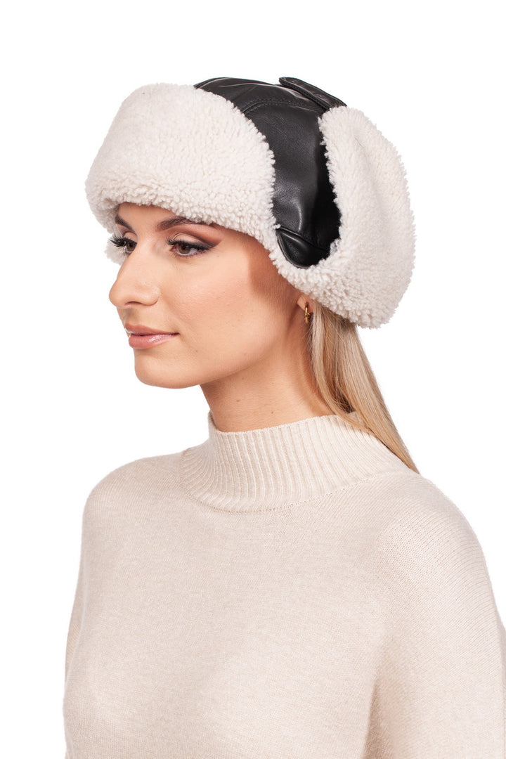 A person wearing a cozy FurbySD White Shearling Fur Aviator Bomber Hat with ear flaps contrasts strikingly with their light-colored turtleneck sweater. The plain white background highlights the unique style of the headwear.