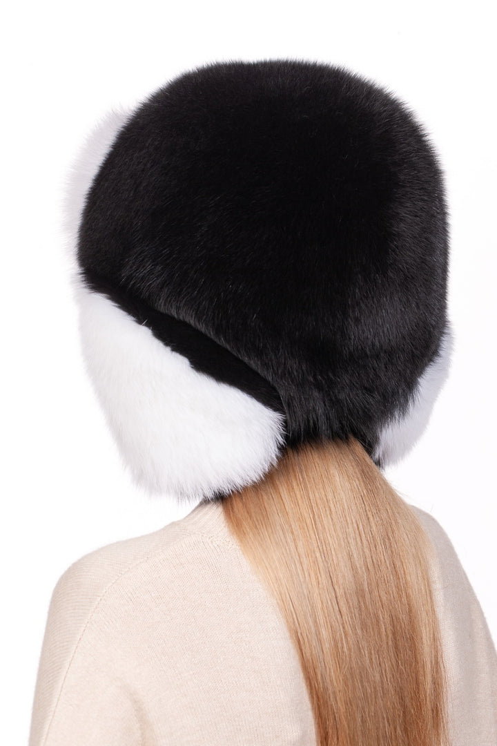 Dressed in the FurbySD Fox Fur Ushanka Trapper Hat, featuring large ear flaps and a stylish black and white design, a person exemplifies a winter essential. Their long, straight hair falls gracefully below the hat as they turn away, enveloped in a cozy beige sweater against the simple white background.