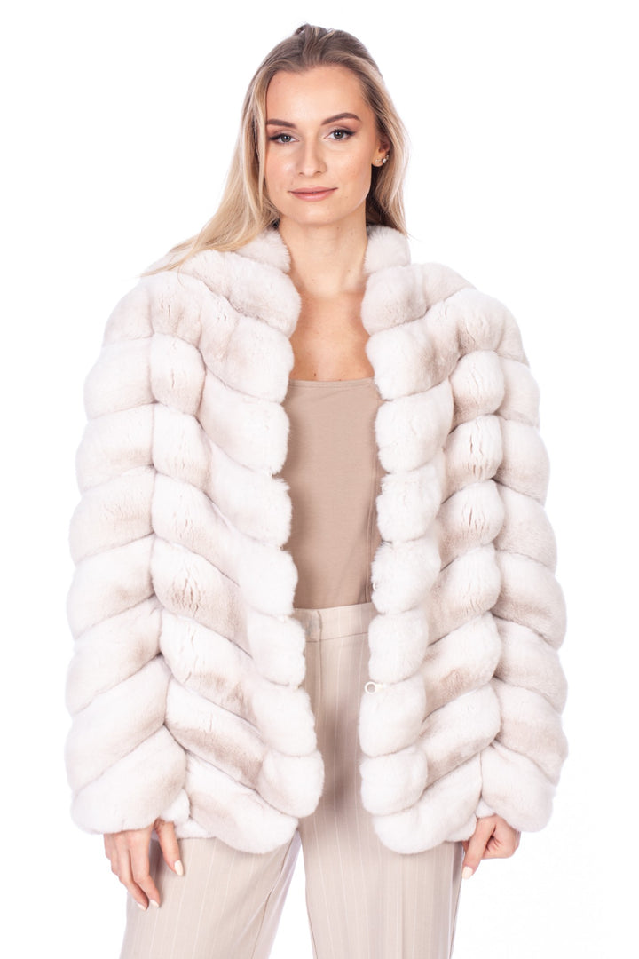 A person with long blond hair wears a sophisticated Cream Chinchilla Fur Coat by FurbySD over a beige top and light-colored pants, exuding elegance. They are posing against a plain white background.