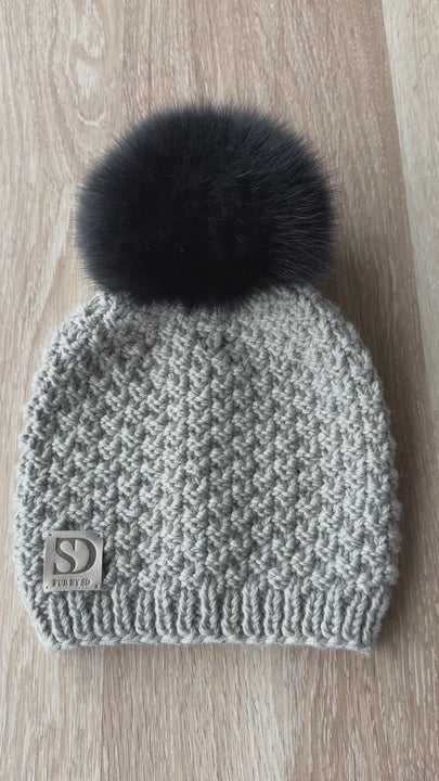 Greyish beige merino wool beanie with black fox fur pom pom on model, hand knitted winter hat for women, luxury fur bobble hat