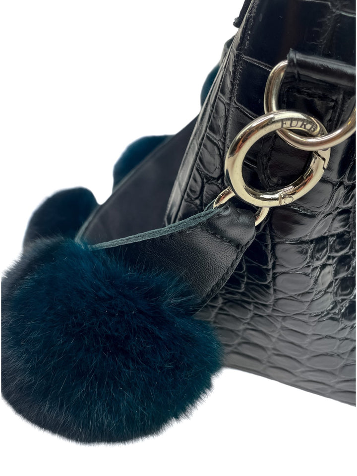 Close-up of the Chinchilla Fur Bobble Bag Strap by FurbySD, featuring a furry teal pom pom accessory made from ethically sourced fur. The black textured handbag boasts a shiny, crocodile-like pattern with metallic rings attaching the strap to the bag. The image highlights the luxurious details and texture of this exquisite piece.