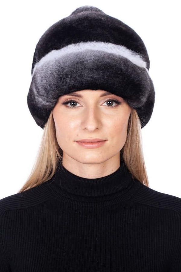 A person wearing a luxurious FurbySD Chinchilla Fur Hat With Pom Pom and a black turtleneck stands against a plain white background. The soft, handmade winter accessory from Lithuania adds an elegant touch.