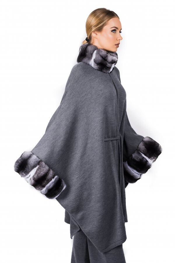 An individual is styled in the Chinchilla Fur Trim Cashmere Cape Poncho by FurbySD, featuring elegant chinchilla fur accents on the collar and sleeves. The ensemble is completed with coordinating pants. The individual, with blond hair tied back, stands posed against a simple white backdrop.