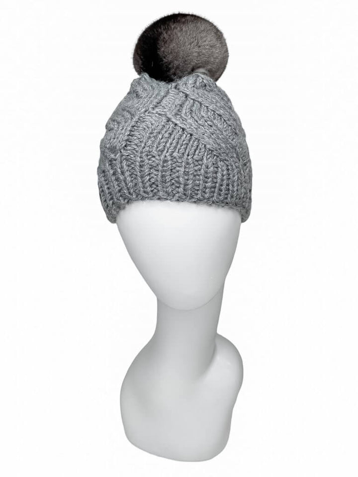 A Grey Chinchilla Fur Beanie by FurbySD, featuring a large, fluffy pom-pom on top, handmade in Lithuania, is displayed on a white mannequin head against a plain background.