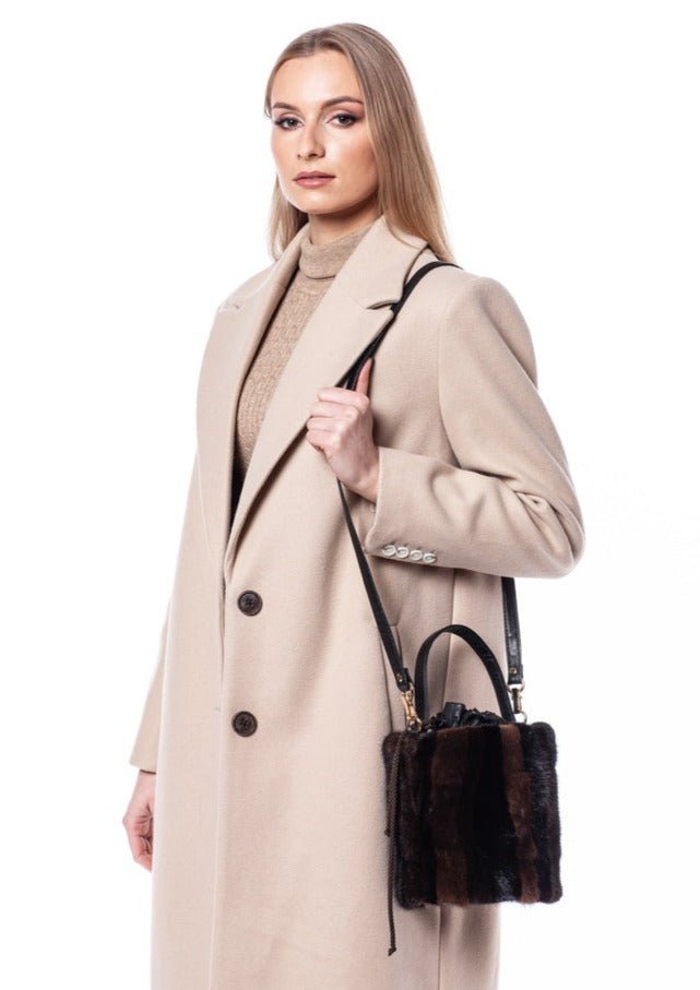 A woman with blonde hair is wearing a beige overcoat and holding a FurbySD Mink Fur Cylinder Handbag. She is standing against a plain white background, looking directly at the camera with a neutral expression.