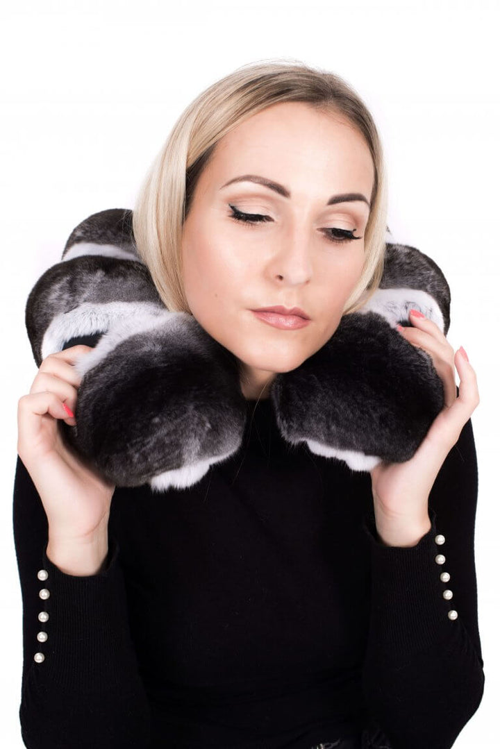 A person with closed eyes is comfortably wearing the FurbySD Chinchilla Fur Travel & Neck Support Cushion. The individual has short blond hair and is dressed in a black top with button details on the sleeves, set against a plain white background that enhances the serene mood.